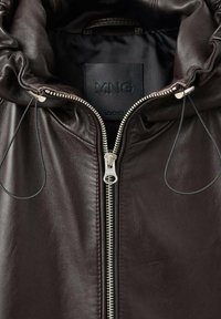 Giacca di pelle marrone scuro con collo alto, zip metallica e etichetta interna nera con il nome del marchio "MNG."