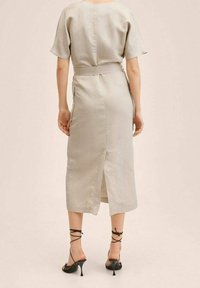 Robe beige clair à manches courtes, taille cintrée et fente à l'arrière ; fabriquée en tissu lisse, complétée par des talons noirs à brides.