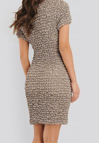 Getailleerde, gerimpelde jurk in beige met korte mouwen en textielstructuur. Knielang ontwerp benadrukt de ingewikkelde rimpeldetails.