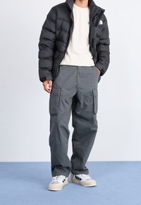 Svart puffjacka med dragkedja, krämfärgad t-shirt under, grå cargobyxor med fickor och grå sneakers med vita detaljer.