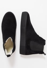Černé semišové kotníkové boty s elastickými postranními panely, texturovanou černou gumovou podrážkou a měkkou vnitřní podšívkou. Obsahují poutko na zadní straně.