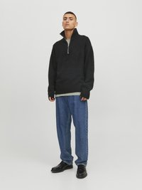 Pull à col zippé noir avec des poignets côtelés, associé à un jean en denim bleu ample et des chaussures noires. Design simple, texture douce et coupe décontractée.