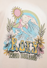 Bēša kokvilnas t-krekls ar krāsainiem grafiskiem elementiem: saule, viļņi, kalni un ziedi. "ROXY" teksts treknā, dzīvīgā krāsā.