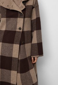 Cappotto di lana a scacchi marrone e beige con un grande colletto, tre bottoni e maniche larghe con una consistenza morbida.