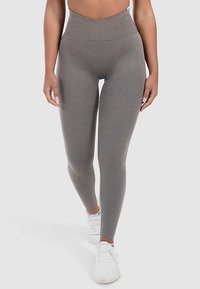 Leggings gris taille haute avec une texture lisse, coupe ajustée et construction sans coutures, accompagnés de chaussures de sport blanches.