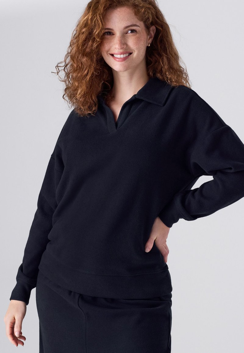 Fekete pulóver puha, texturált anyagból, gallérral és laza szabással. Párosítható hozzá illő sötét alsó ruhadarabbal.