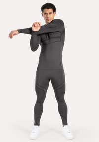 Schwarzes Stretch-Activewear-Set mit langen Ärmeln und enger Passform, ausgestattet mit kantigen Nahtlinien und durchgehendem Texturmuster, kombiniert mit weißen Sneakers.