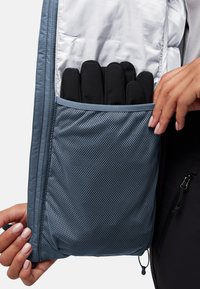 Hellblaue isolierte Jacke mit einem Innenraum, der eine Netzbörse enthält, in der sich fünf schwarze Handschuhe befinden. Glatte und strukturierte Stoffe, mit Reißverschluss und Nähdetails.