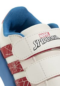 Witte sneaker met een rood spinnenweb ontwerp, blauwe opgevulde kraag en klittenbandsluitingen; heeft het "Marvel Spider-Man" logo prominente weergegeven.