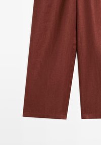 Pantalon à jambes larges couleur rouille, coupé à la cheville, en tissu texturé, présenté sur fond blanc.