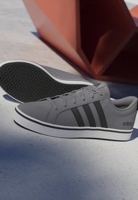 Par de zapatillas Adidas grises con rayas negras y suelas blancas, un zapato está tumbado de lado mostrando la suela con patrón de panal.