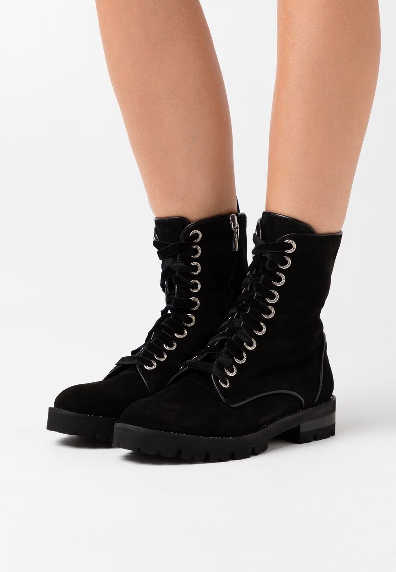 Bottines en daim noir avec semelles plates, finition texturée, œillets argentés et lacets. Elles sont dotées d'une fermeture éclair latérale et d'un accent noir contrastant.