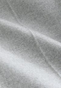 Gros plan d'un tissu texturé gris clair avec un tissage fin et des plis doux créant des ombres et des reflets subtils.