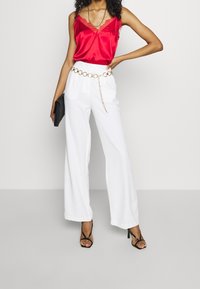 Rød satin cami-top med blondekant, parret med hvide vide bukser med et guld kædebælte. En sort clutch og stiletter med remme fuldender looket.