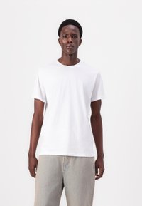 Tricou alb din bumbac, cu mâneci scurte, decolteu rotund și o croială lejeră, asortat cu blugi deschis la culoare.