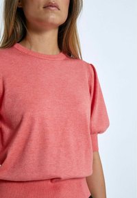 Maglione corto a maniche corte color corallo con scollatura rotonda, orlo a coste e maniche a palloncino; realizzato in morbido tessuto a maglia con una trama mista.
