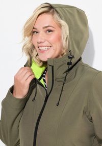 Giacca verde oliva con cappuccio, caratterizzata da una fodera verde neon a contrasto, zip nera e coulisse regolabile per una vestibilità ottimale.