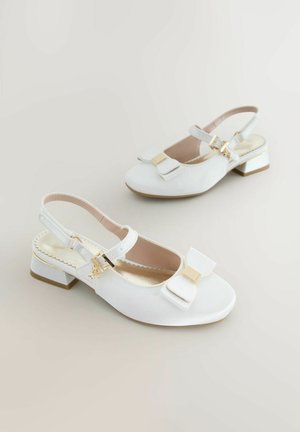 Hvide slingback-sko med rosetdetalje, lavet af glat materiale, med en lille blokhæl med gulddetaljer og en dekorativ spænde.