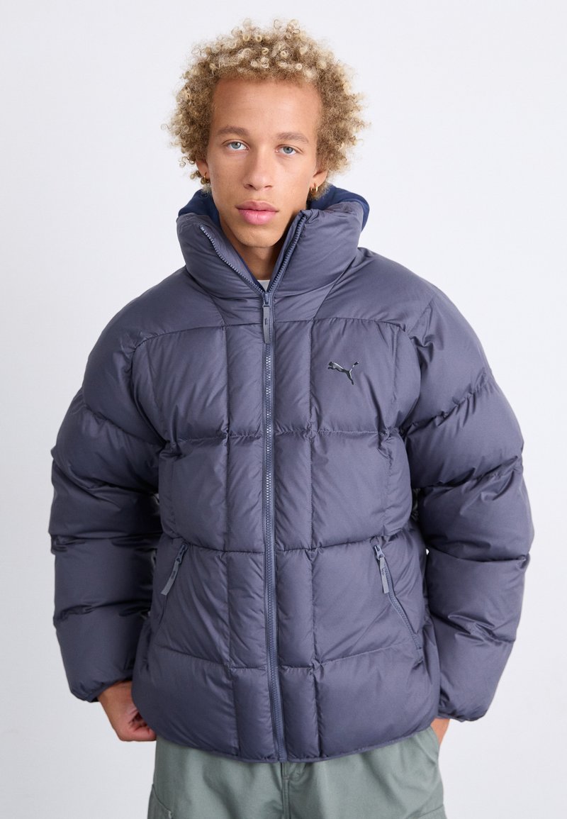 Giacca puffer blu navy con colletto alto, motivo a trapunta, zip frontale e tasche laterali; presenta un piccolo logo sul petto.