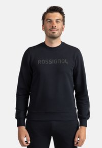 Felpa nera a maglione realizzata in tessuto morbido con polsini e orlo a coste. Presenta un audace logo "ROSSIGNOL" centrale in colore a contrasto.