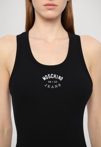 Čierny rebrovaný tank top s okrúhlym výstrihom a bielym logom "MOSCHINO JEANS 86-23" na prednej strane. Hladká textura, priliehavý strih.
