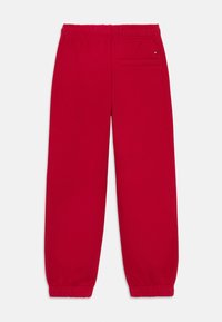 Rode sweatpants van zacht materiaal, met een elastische tailleband, afgeknipte enkels en een achterzak met subtiele merkdetails.