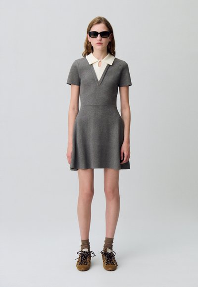 Robe grise à manches courtes avec un décolleté en V profond et un col crème. Associée à des chaussures marron et des chaussettes beiges. Texture lisse, style décontracté.