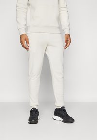 Cream hoodie with front pocket and matching cream tapered joggers. Worn with black athletic shoes featuring white accents.