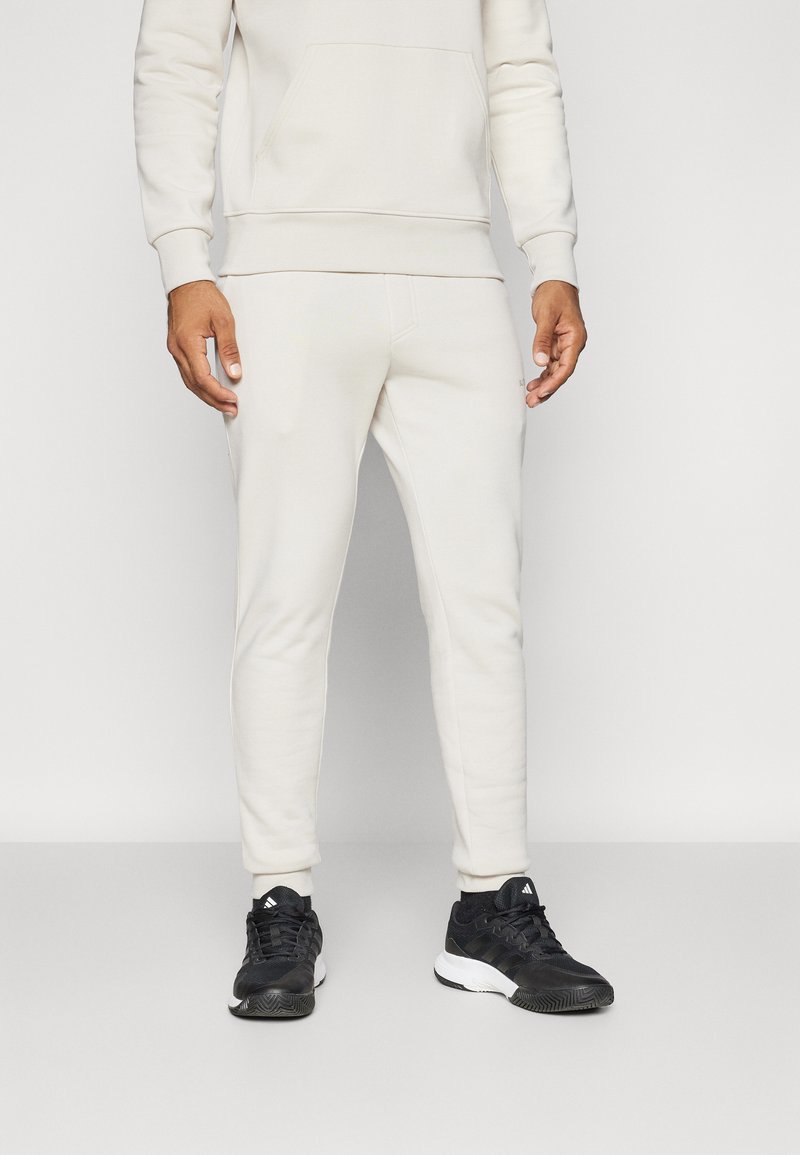 Creme hoodie med frontlomme og matchende creme tapered joggers. Båret med sorte atletiksko med hvid detaljer.