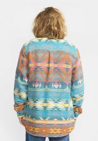 Multikleurige, gebreide blouse met patronen, featuring geometrische ontwerpen in blauw, oranje, roze, geel en crème. Lange mouwen met een afgeronde zoom.