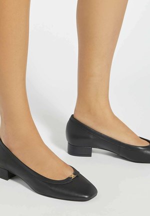 Ballerines en cuir noir avec bout carré, petit talon carré et un accent doré à l'avant. Texture lisse avec une finition polie.