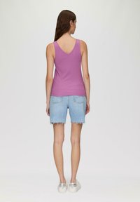 Fioletowy ribbed tank top z dekoltem w kształcie litery V, zestawiony z jasnoniebieskimi szortami dżinsowymi z postrzępionymi brzegami. Modelka nosi srebrne buty na platformie.