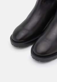 Bottes courtes en cuir noir à finition lisse, bouts arrondis, semelles en caoutchouc texturées contrastantes, avec un design à profil bas.