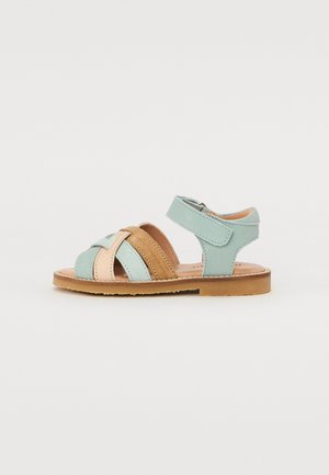 Myntegrønn og beige lær sandaler med kryssede stropper, justerbar spenne, og en brun gummisåle. Har glatt tekstur og klassisk design.