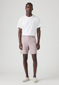 Tricou alb din bumbac asociat cu pantaloni scurți roz deschis, evidențiind un design simplu, o croială lejeră și un stil clasic cu cinci buzunare.