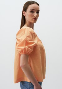 Blouse à manches courtes, couleur orange clair, avec un col froncé et des manches bouffantes. Fabriquée en coton lisse, elle offre une coupe décontractée.