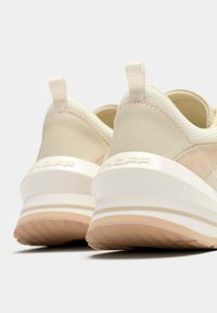 Zapatillas deportivas beige con parte superior texturizada, suela media blanca y detalles en tono rosado claro. Tacón redondeado con un patrón sutil de agarre.