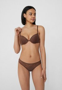 Hnědá krajková podprsenka s tvarovanými košíčky a tenkými ramínky, v kombinaci s odpovídající krajkovou tangou. Obě mají květinové vzory a jemnou texturu.
