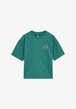 Tricou verde cu mâneci scurte și guler rotund, confecționat dintr-un material texturat, cu un mic patch în formă de diamant pe partea stângă a pieptului inscripționat cu „Soare și Distracție”.