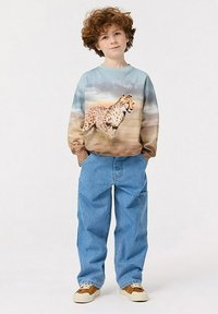Felpa a maniche lunghe con una grafica di ghepardo in tonalità di blu e marrone, abbinata a jeans blu dalla vestibilità morbida e sneakers beige.