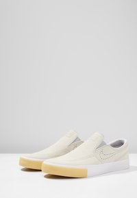 Chaussures à enfiler en toile crème avec une finition texturée, semelles en caoutchouc blanches et détails perforés subtils sur les côtés.