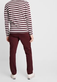 Långärmad maroon- och vitrandig skjorta i kombination med maroon byxor; skjortan har horisontella ränder och en rund halsringning.