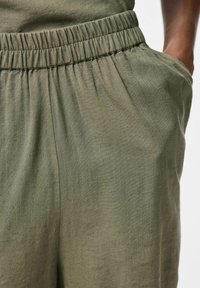 Pantaloni corte verde oliva con cintura elasticizzata, caratterizzati da una texture morbida e tasche laterali, che mostrano un design casual e rilassato.