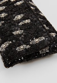 Tissu noir avec des sequins noirs brillants et des perles argentées disposés en petits motifs losanges.