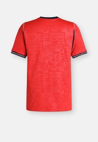 Κόκκινη αθλητική φανέλα με κοντά μανίκια και διακριτικά αφηρημένα μοτίβα, ναυτικό γιακά και άκρες μανικιών με λευκές και κόκκινες ρίγες, εμφανιζόμενη από πίσω.