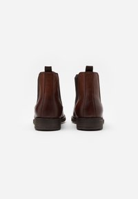 Bottines Chelsea en cuir marron avec des panneaux latéraux élastiques, bout arrondi et talon empilé bas. Texture lisse et design simple.
