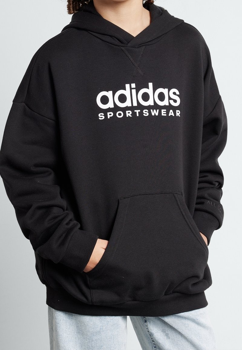 Černá mikina s kapucí z bavlněné směsi, s přední kapsou typu klokanka a bílým logem "adidas sportswear" na hrudi.