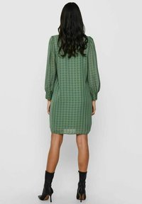Vihreä ruudullinen mekko puffihihnoilla, läpikuultavalla kankaalla ja muotoilevalla siluetilla, yhdistettynä mustiin korkokenkiin. Yksinkertainen ja tyylikäs muotoilu.