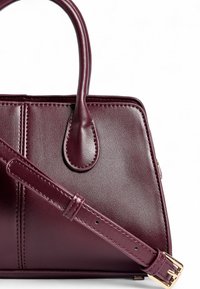 Burgundijas krāsas ādas rokassoma ar divām rokturiem, noņemamu siksnu un izšuvumiem. Gluda tekstūra ar zelta tonī apdares elementiem.