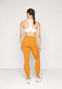Hvit sports-bh og oransje high-waisted leggings, som viser en jevn tekstur, tettsittende fasong og en flettet frisyre.